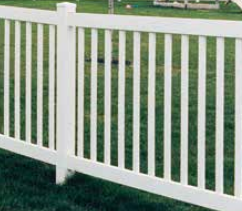 White vinyl picket fence with a square post set in front of a green grass lawn.