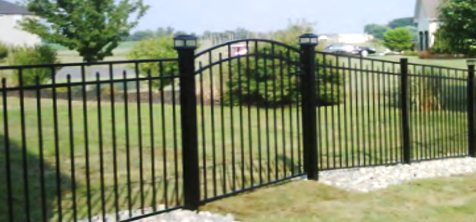 Black metal fence with an arched gate, featuring post cap lights in a grassy, suburban residential yard.