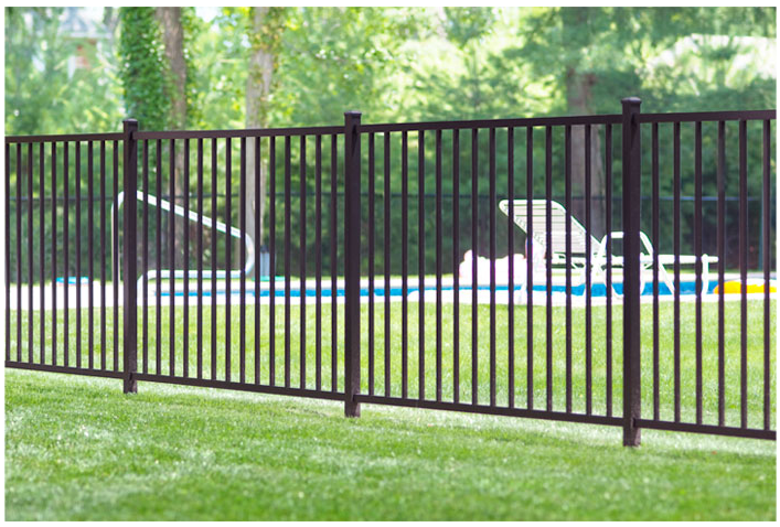 A brown metal picket fence encloses a grassy backyard with a swimming pool and lounge chair in the background.