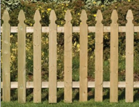 A wooden picket fence with pointed tops set against a blurred background of green foliage and yellow flowers.