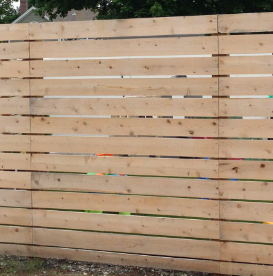 A light-colored horizontal wood plank fence with small gaps between each board, set against a blurred outdoor background.