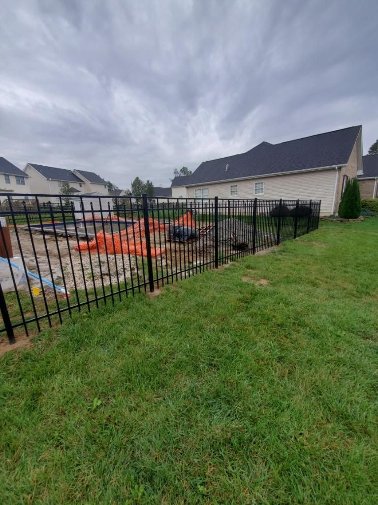 A black metal fence encloses a backyard construction site with orange safety mesh on a cloudy day.