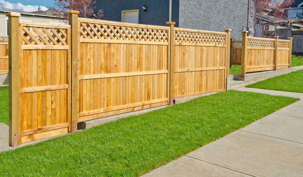 A wooden privacy fence with a lattice top section runs along a grassy area next to a concrete sidewalk.