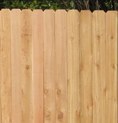 A close-up view of a new wooden privacy fence featuring natural, light-brown vertical pickets with dog-eared tops.