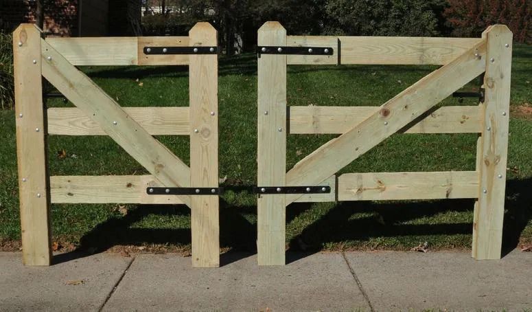 Two light-wood farm gates side-by-side with black metal hinges, set against a green lawn and concrete pavement.