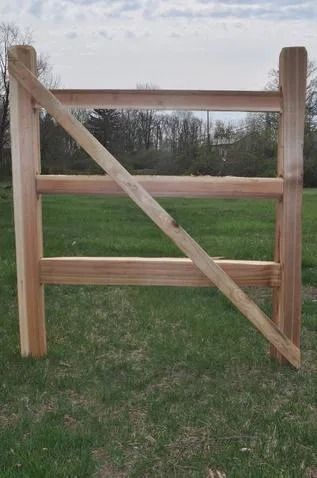 A wooden gate frame with a diagonal support brace standing in a grassy field.