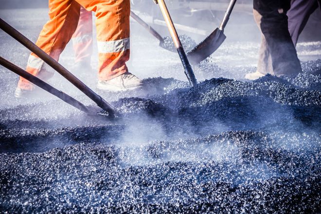 Workers using shovels to spread hot asphalt on a road surface