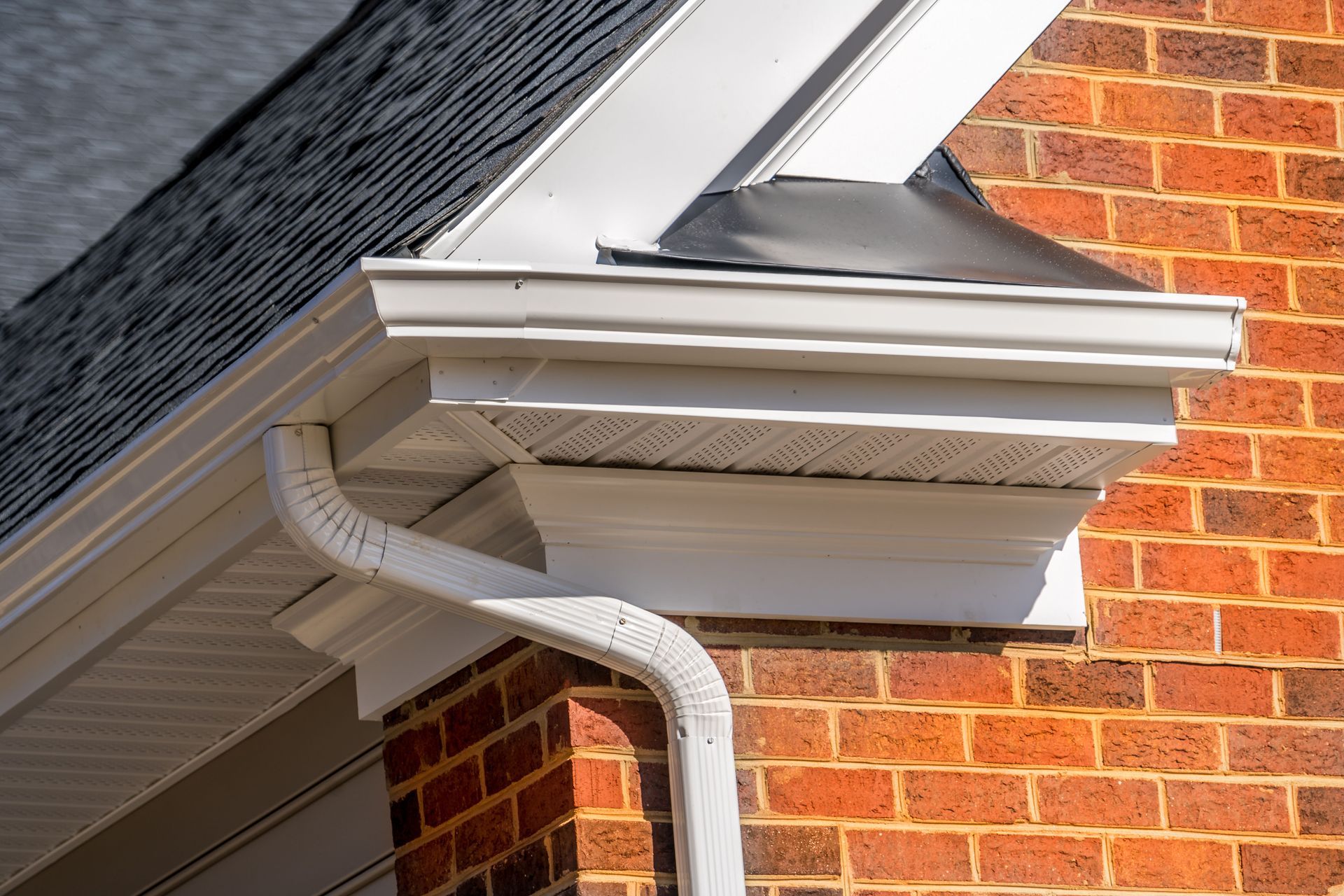 White gutter downspout on brick house under gray roof eave