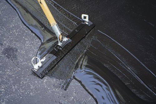 Broom sweeping black tar or wet asphalt on a road surface
