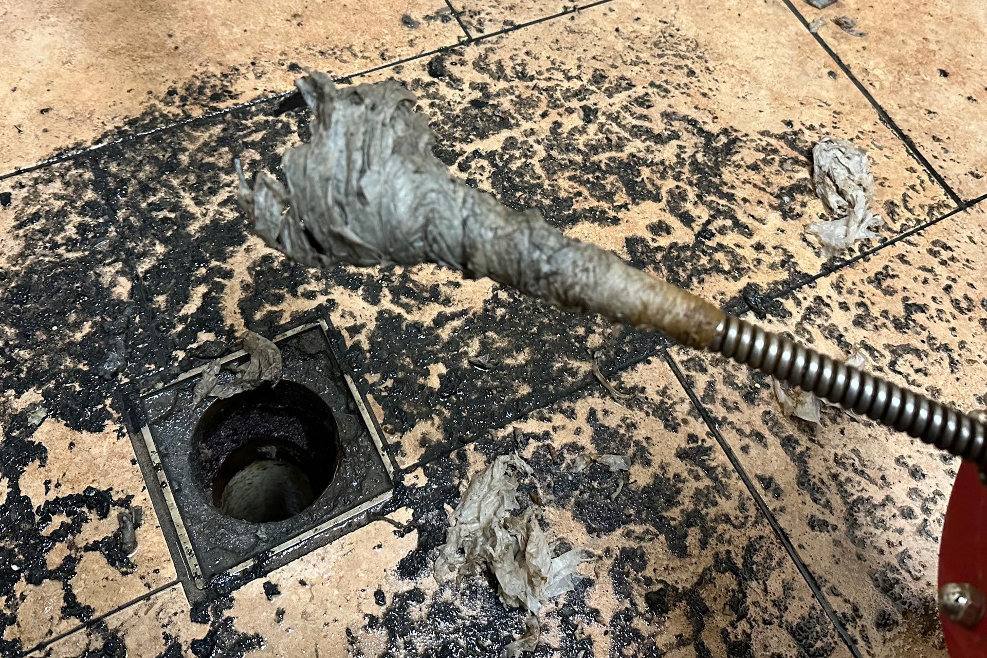 a drain with a hose sticking out of it on a tiled floor