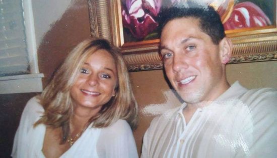 Two people smiling indoors on a couch, with a framed picture behind them.