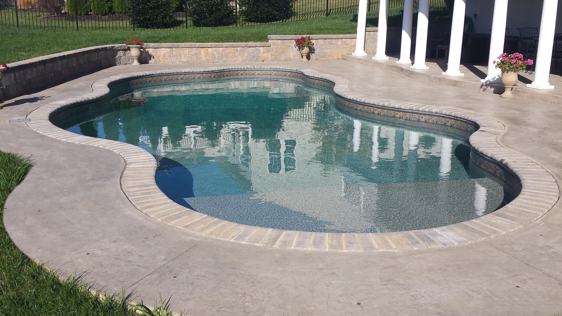 A large swimming pool is surrounded by a concrete patio and a stone wall.