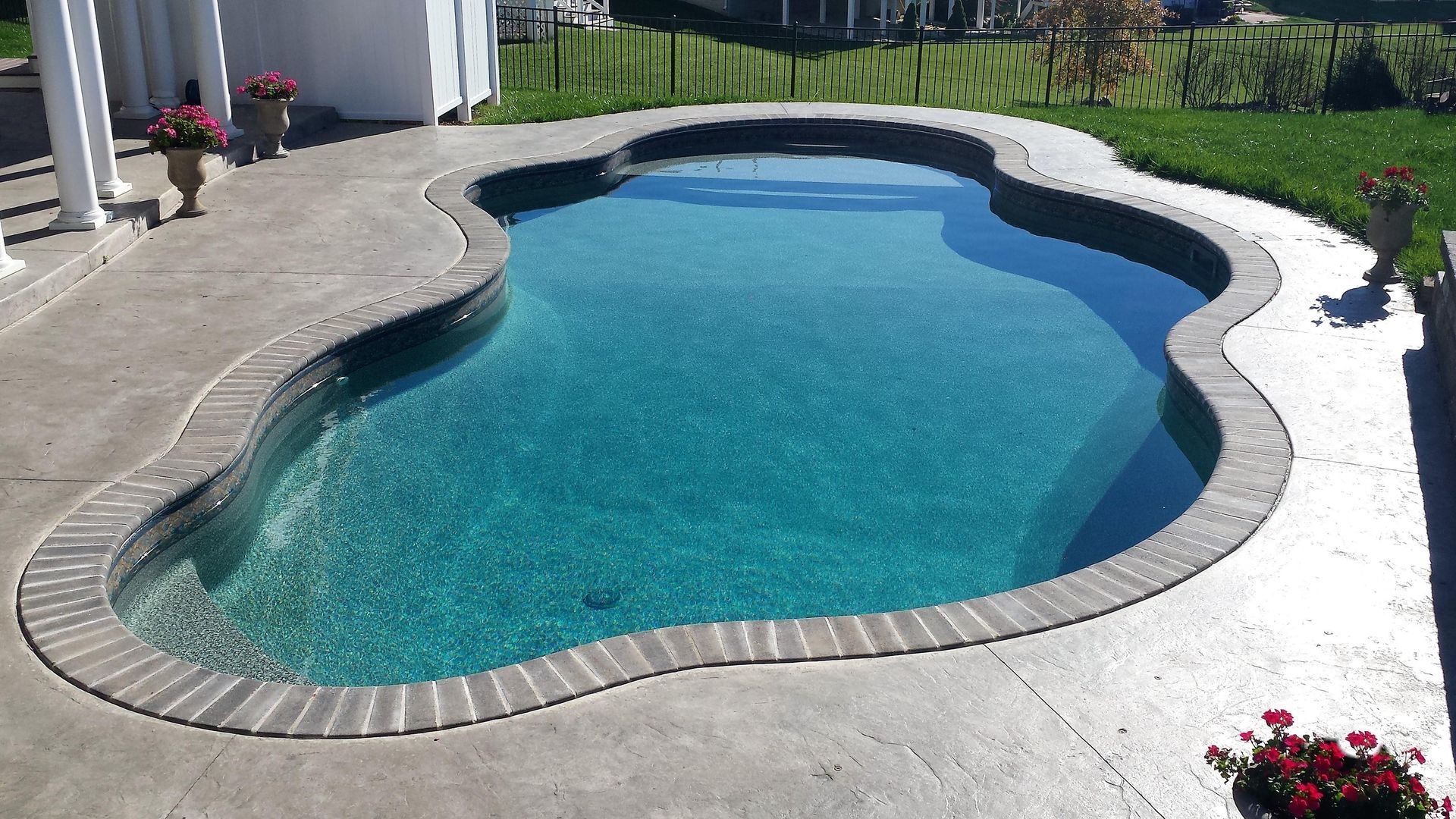 A large swimming pool is surrounded by a brick patio