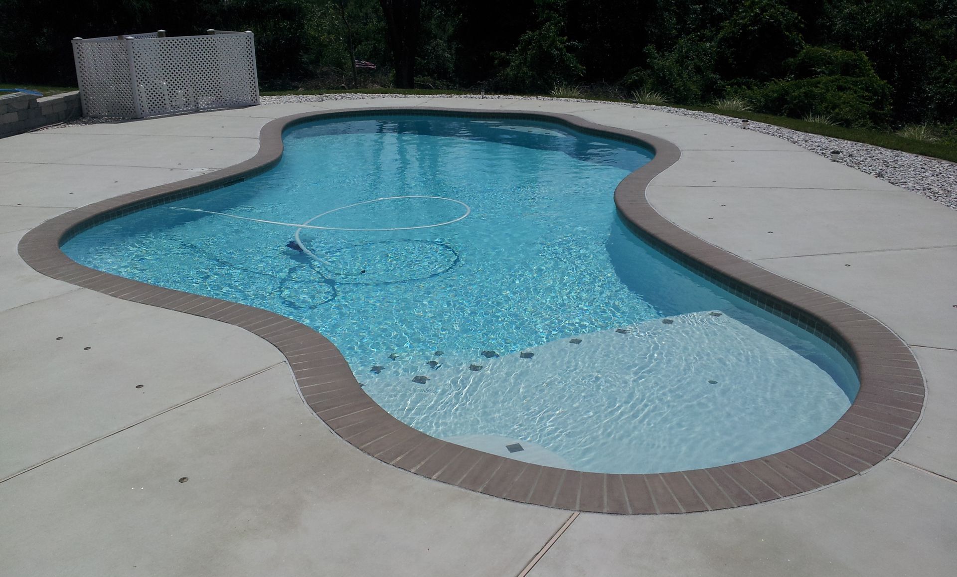 A large swimming pool with a brick border and a concrete deck