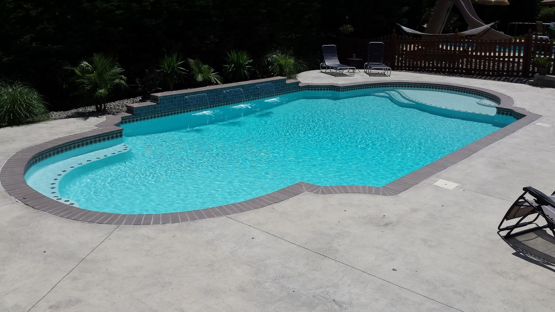 A large swimming pool is surrounded by chairs and a fence.