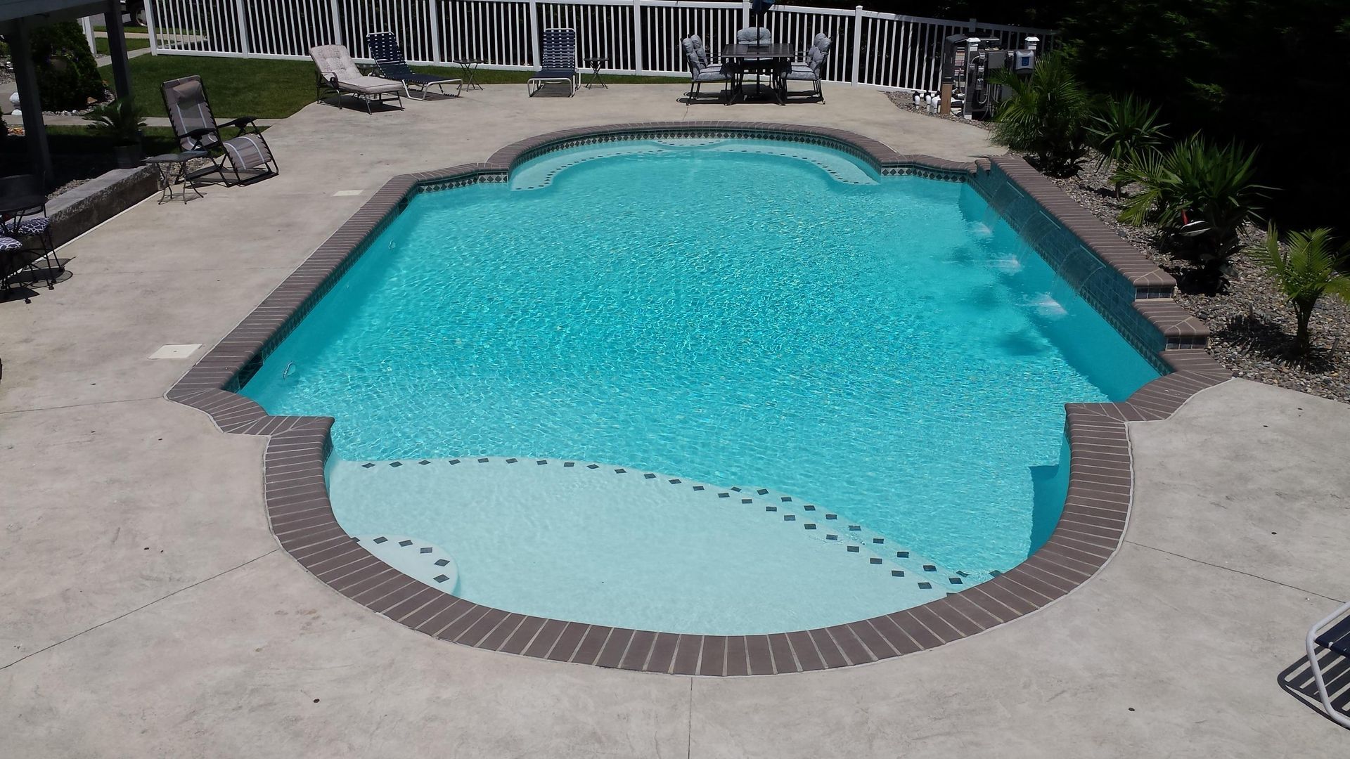 A large swimming pool with a brick border and chairs around it