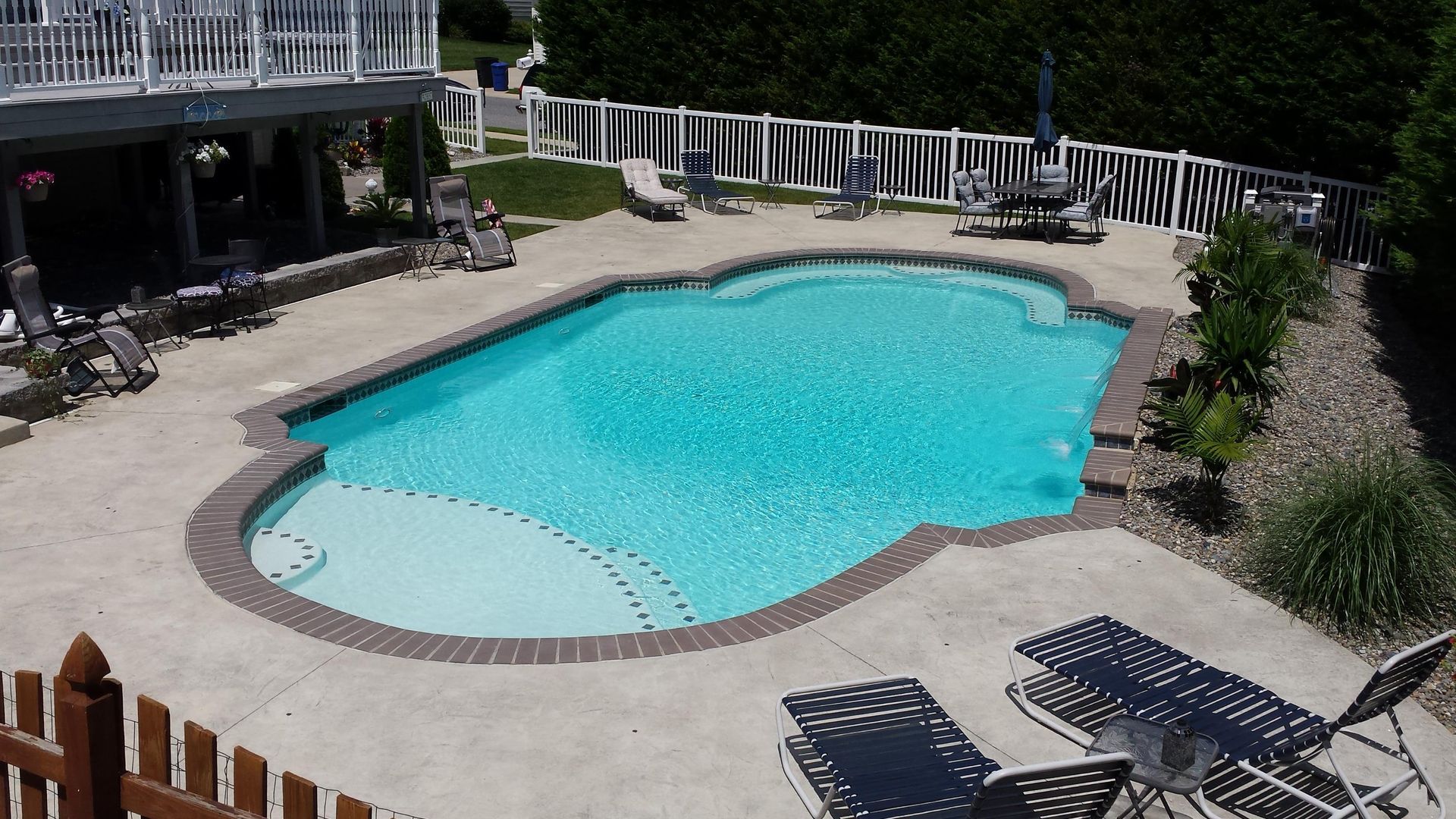 A large swimming pool is surrounded by chairs and a fence
