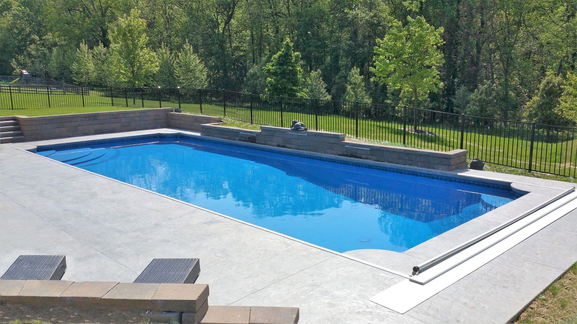 A large swimming pool is surrounded by trees and a fence.