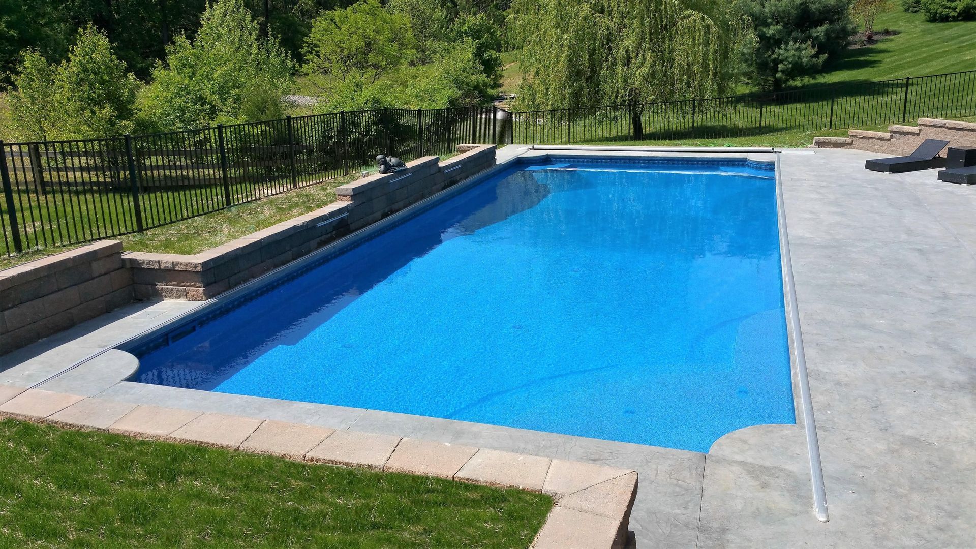 A large blue swimming pool is surrounded by a fence and lawn.