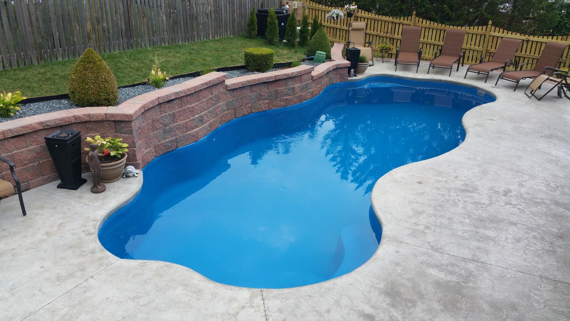 A large blue swimming pool is surrounded by chairs and a brick wall.