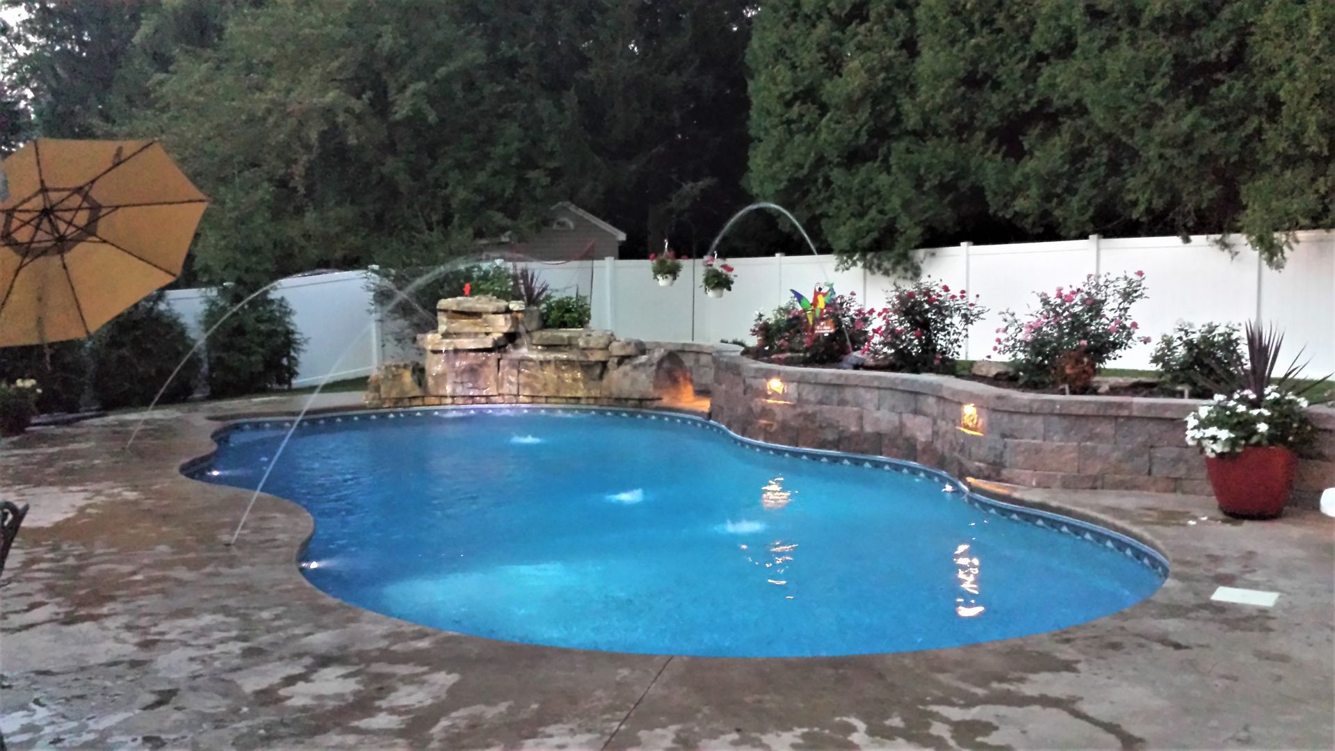 A large swimming pool with a waterfall and a yellow umbrella