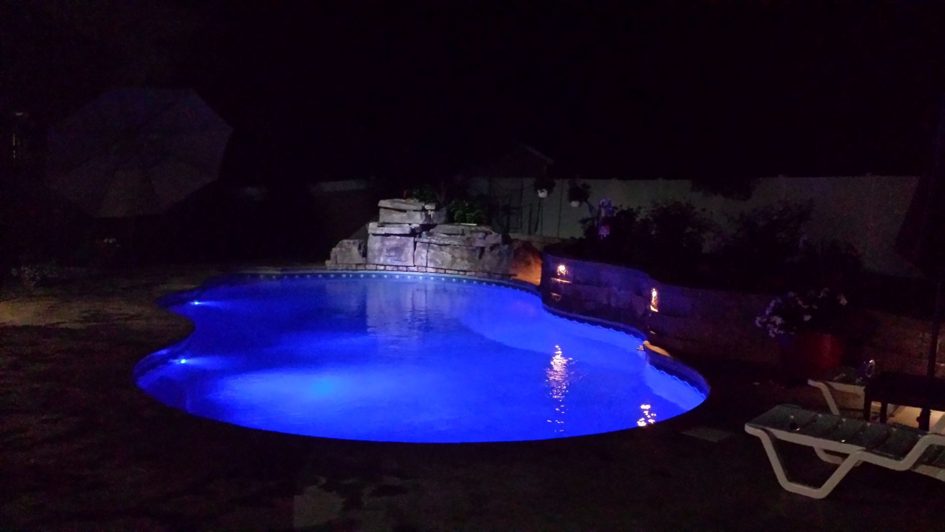 A large swimming pool is lit up at night with blue lights.