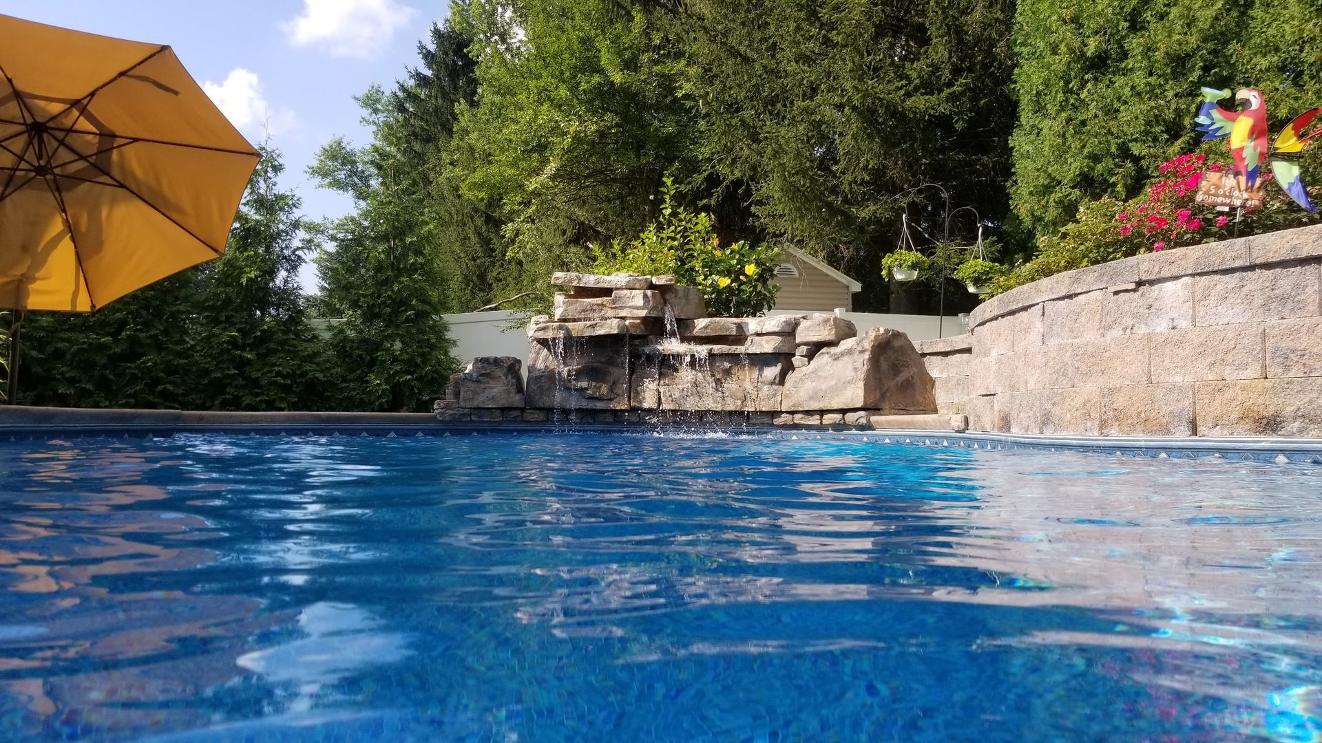 A swimming pool with a yellow umbrella and a waterfall in the background.