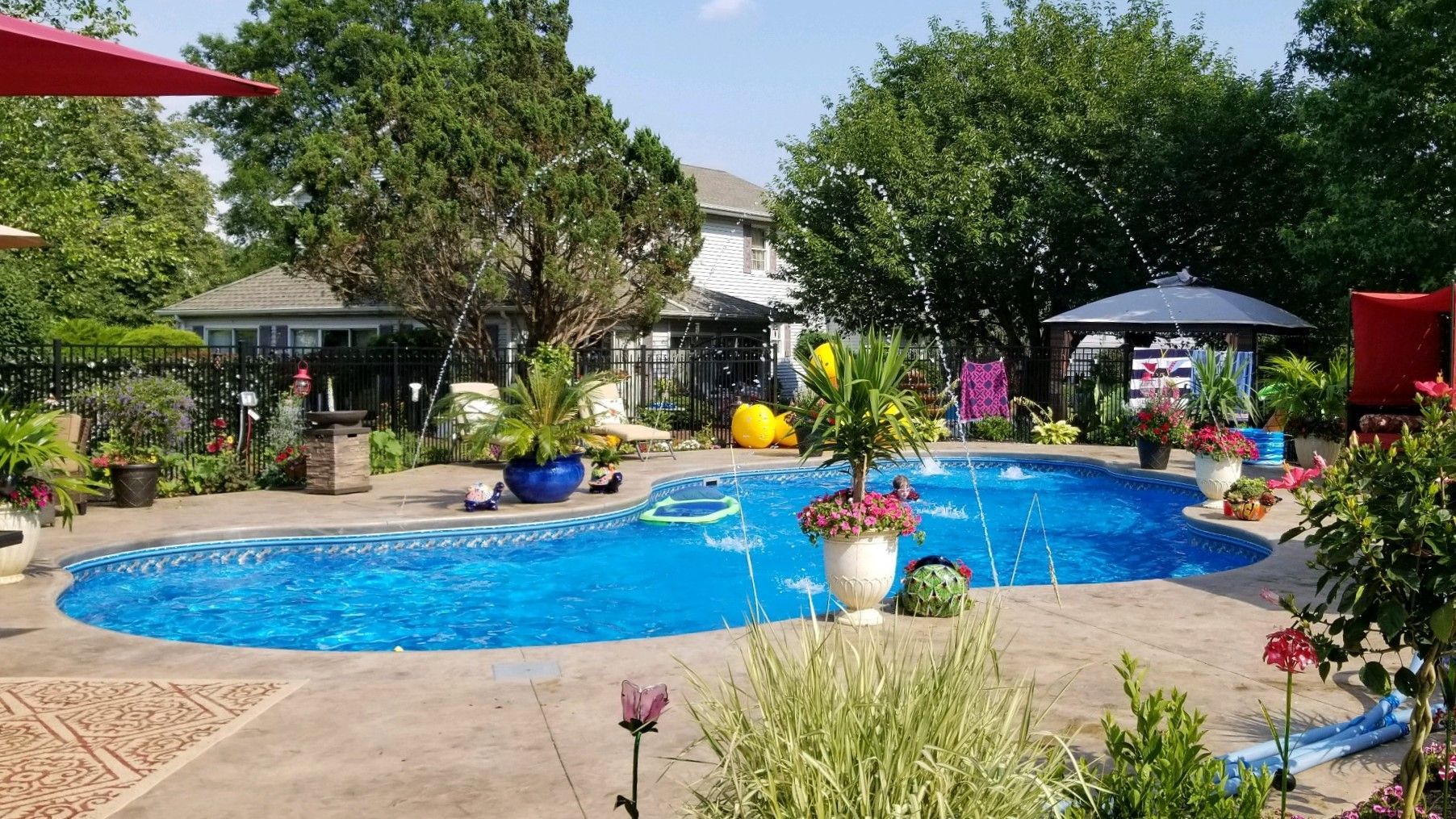 A large swimming pool surrounded by trees and flowers in a backyard.