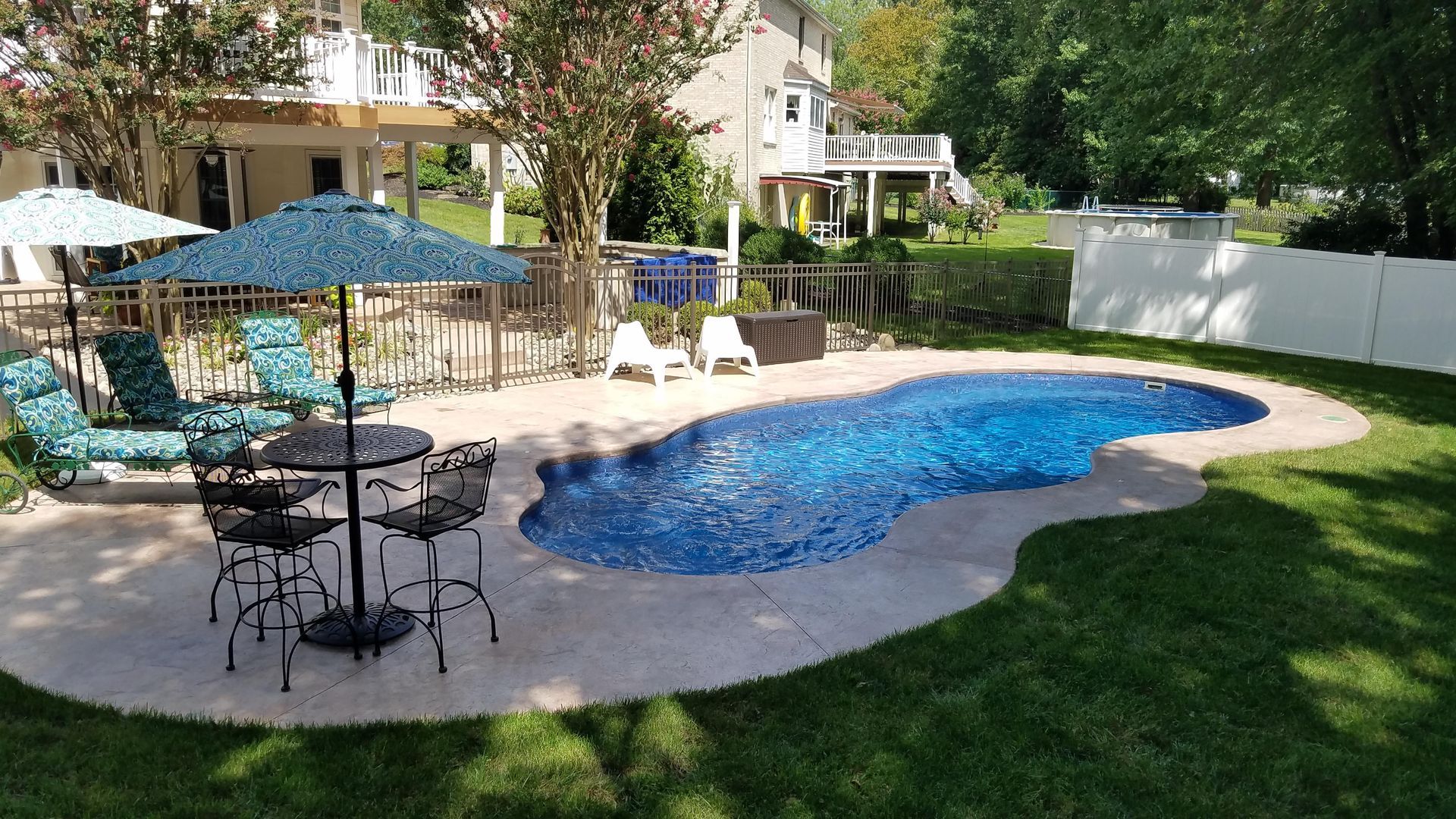 A large swimming pool in a backyard with a table and chairs and umbrellas.