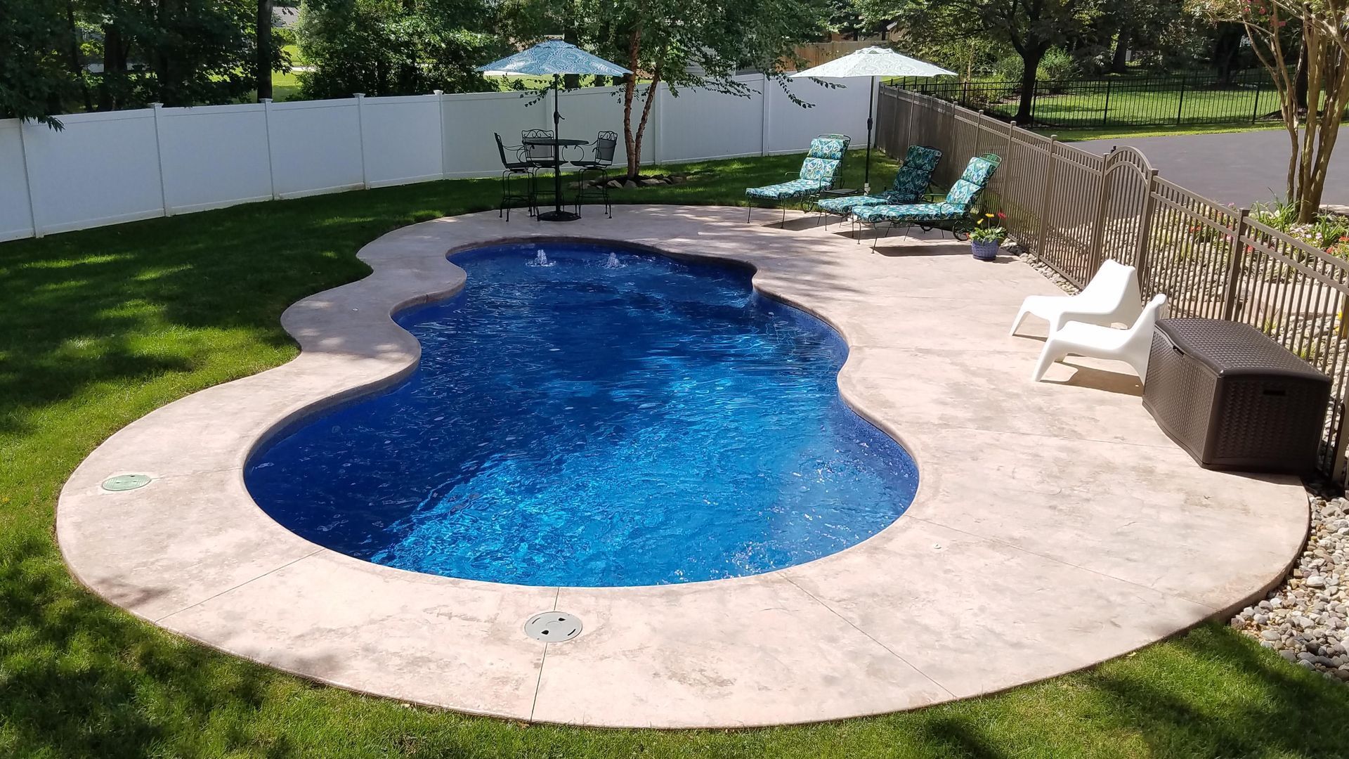 A large swimming pool is surrounded by lawn chairs and a white fence