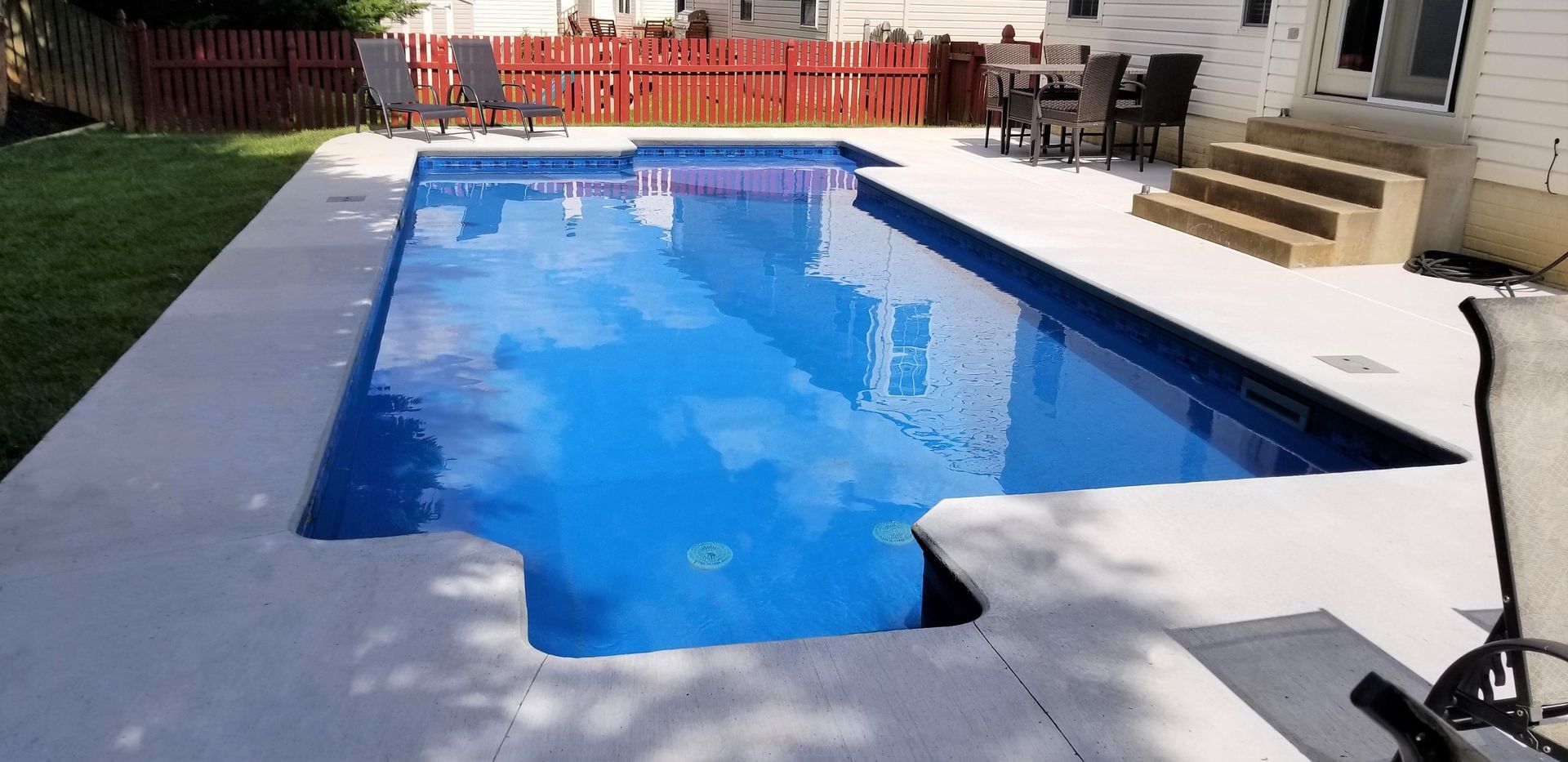 A large swimming pool is in the backyard of a house.
