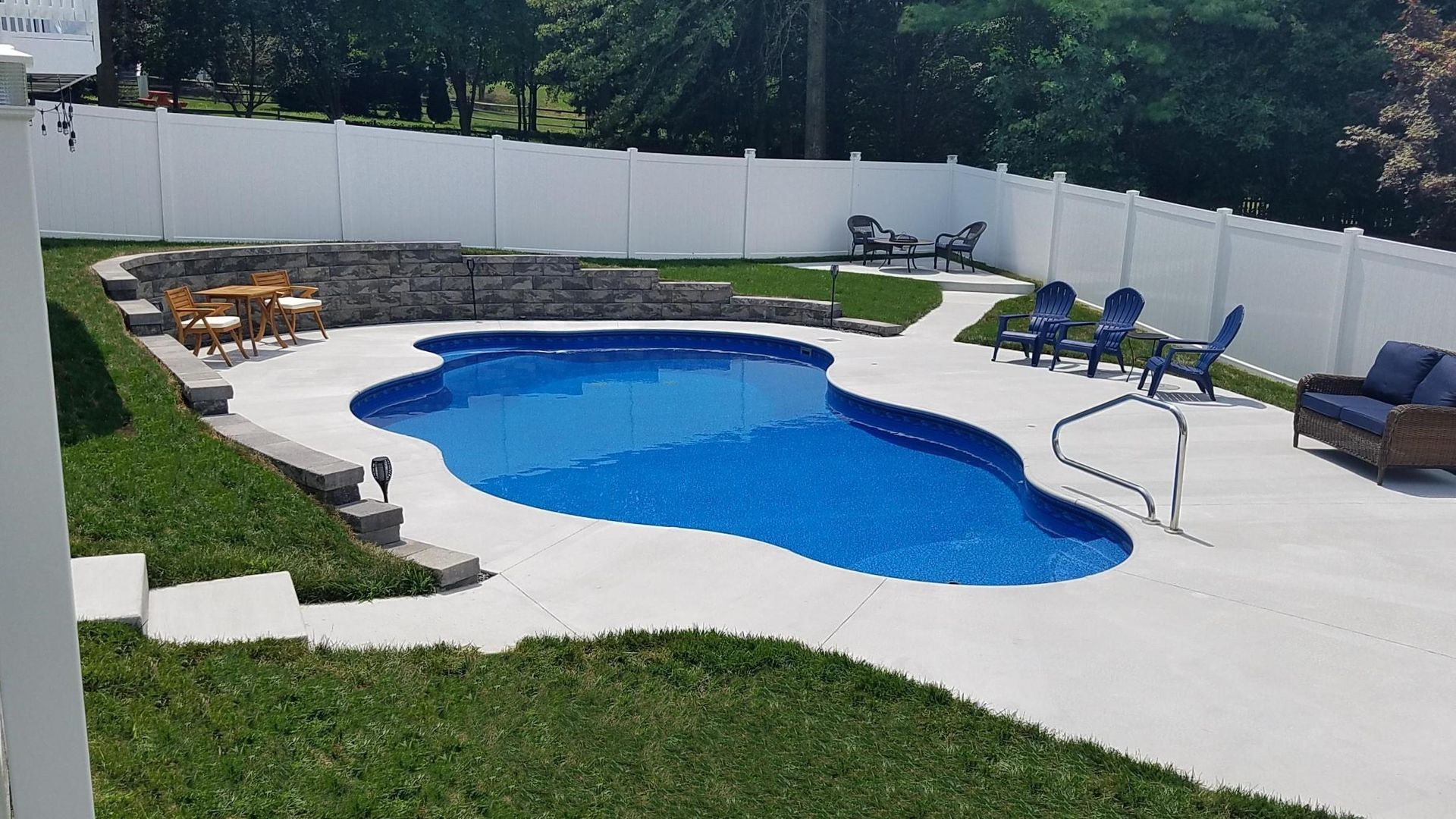 A large swimming pool in a backyard with a white fence surrounding it.
