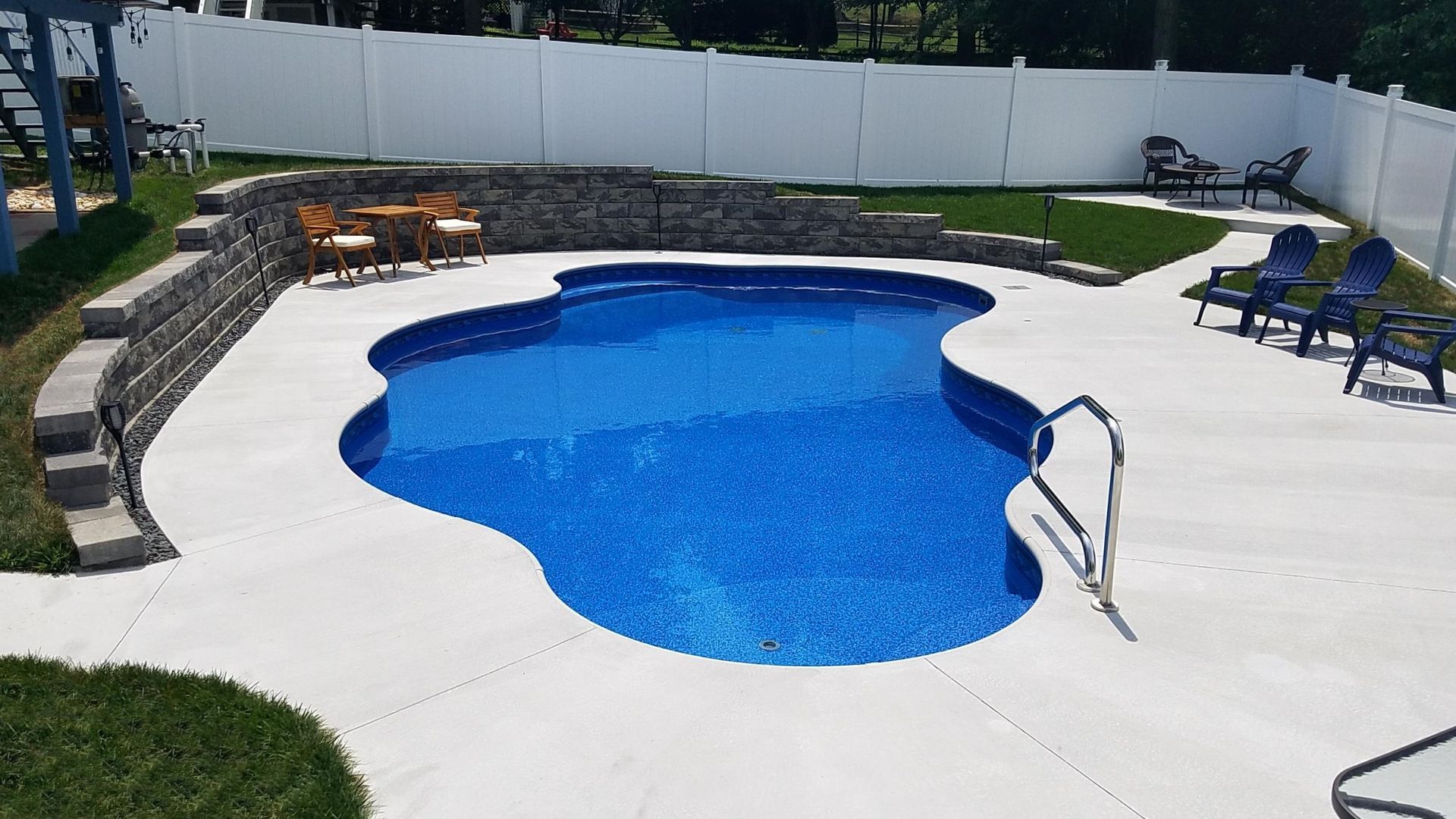 A large blue swimming pool is surrounded by chairs and a white fence.