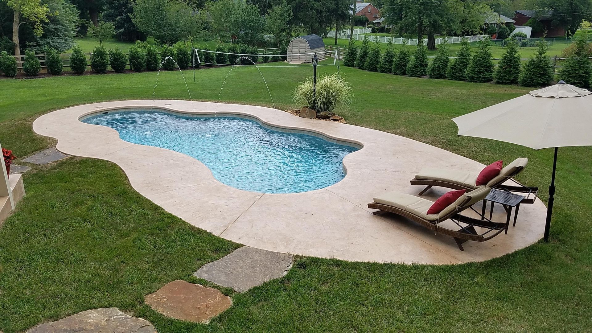 A large swimming pool is surrounded by lawn chairs and an umbrella.