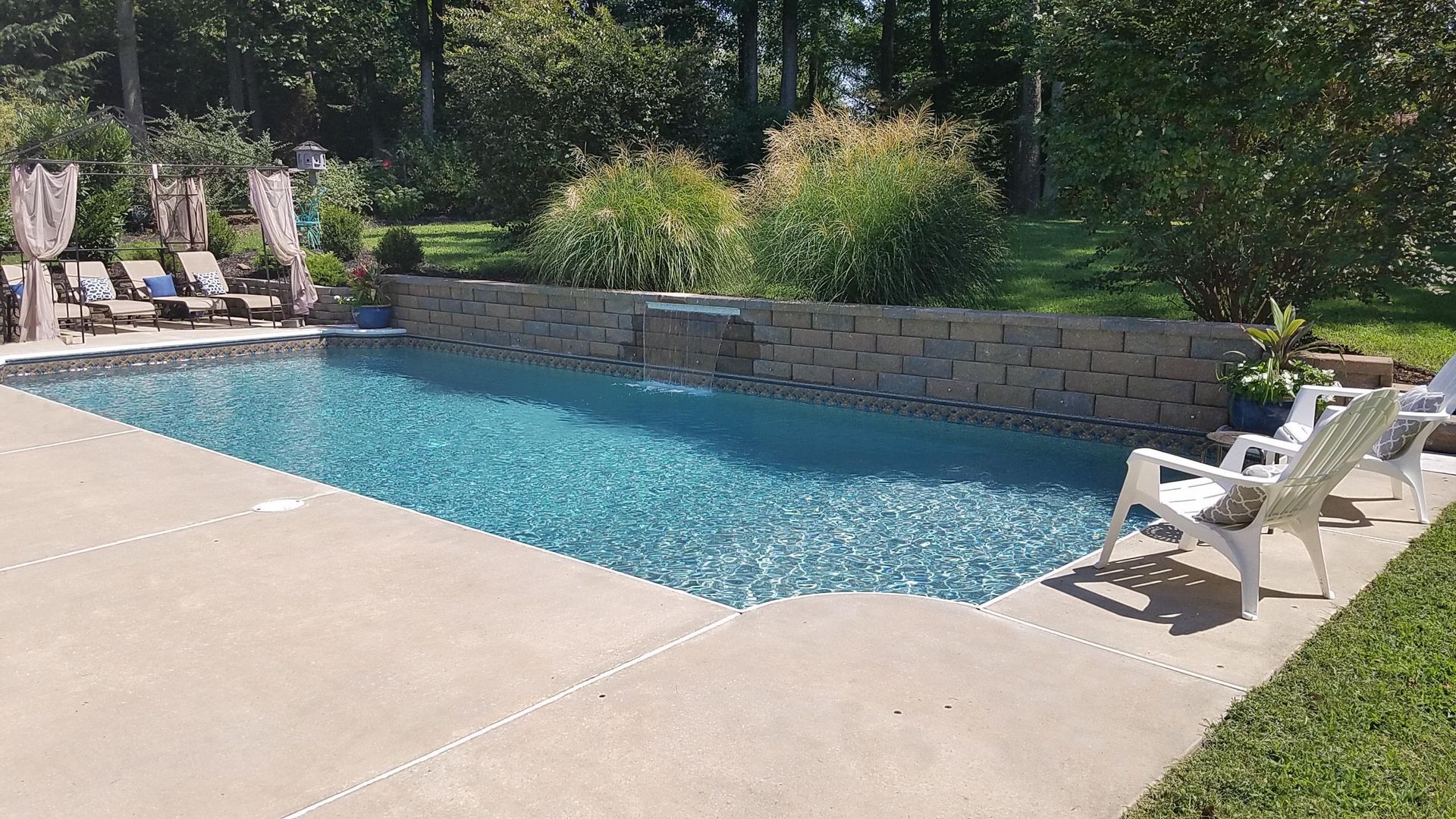A large swimming pool surrounded by chairs and trees in a backyard.