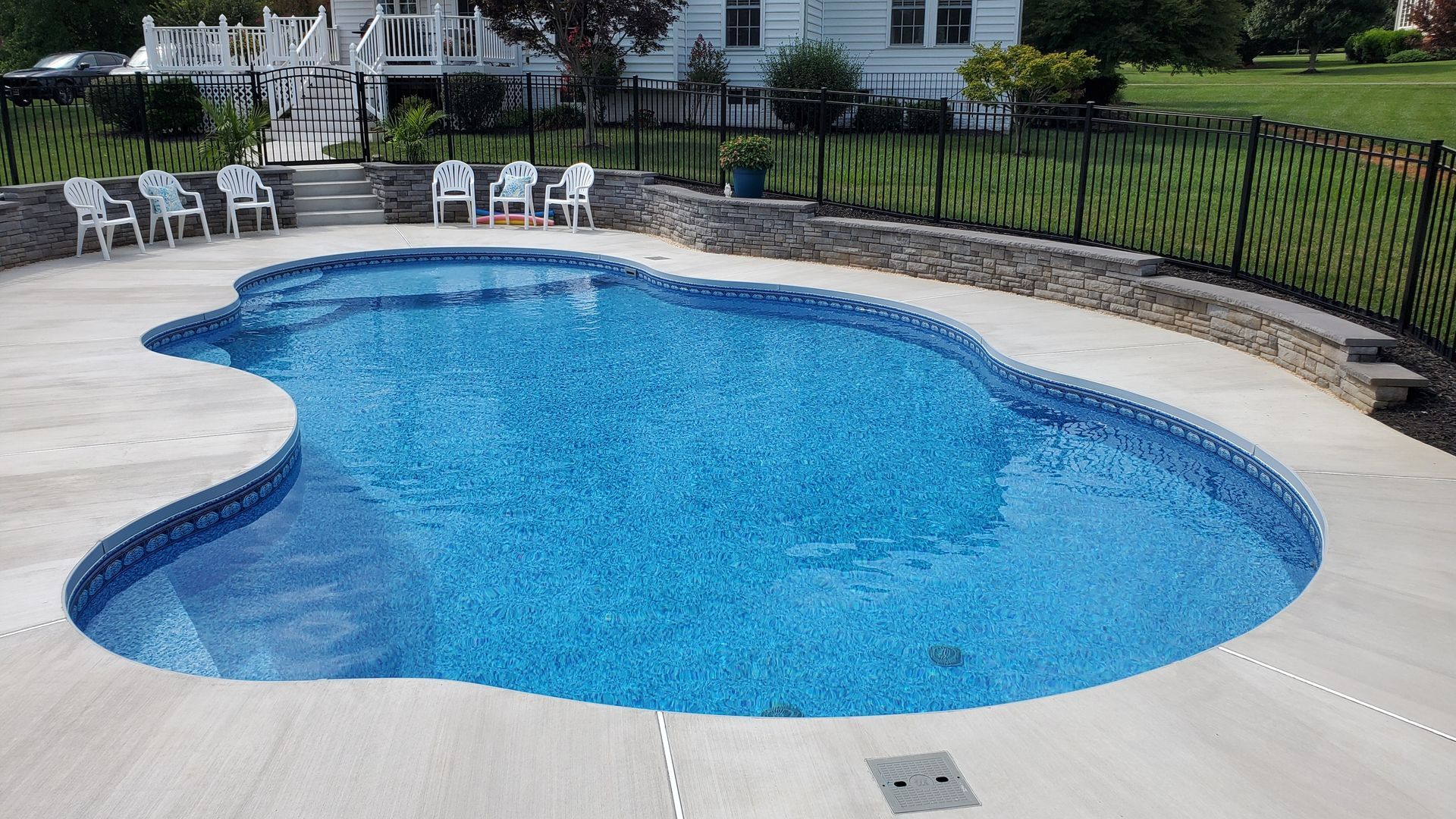 A large swimming pool is surrounded by chairs and a fence.