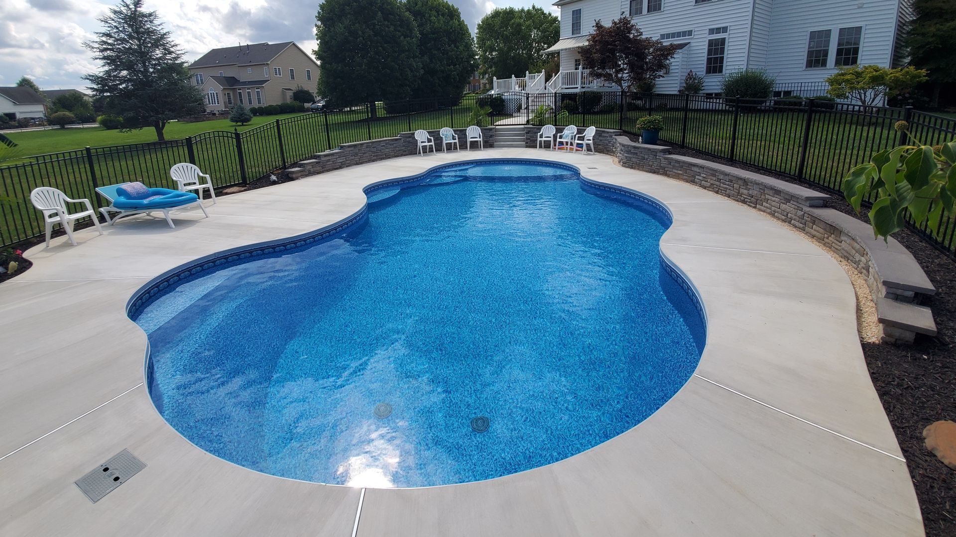 A large swimming pool is surrounded by chairs and a fence.