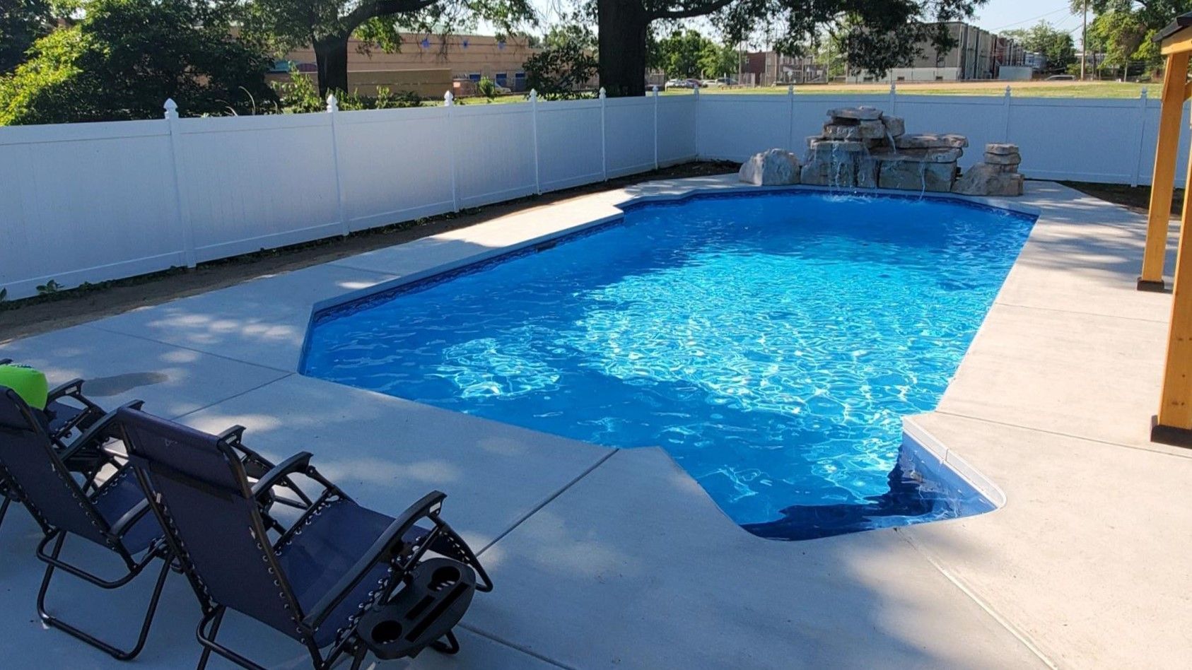 A large swimming pool surrounded by chairs and a white fence.