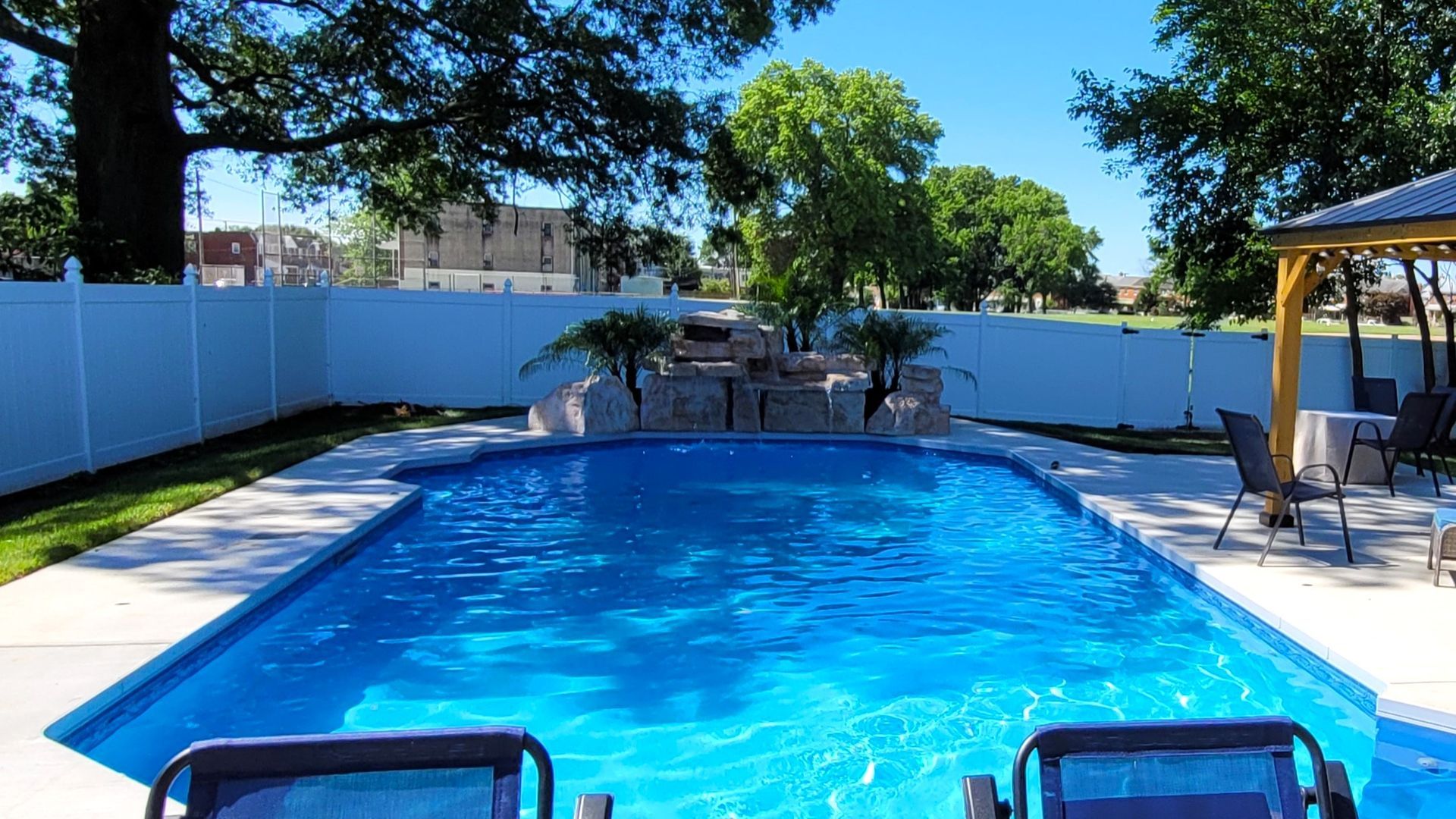A large swimming pool surrounded by chairs and a white fence