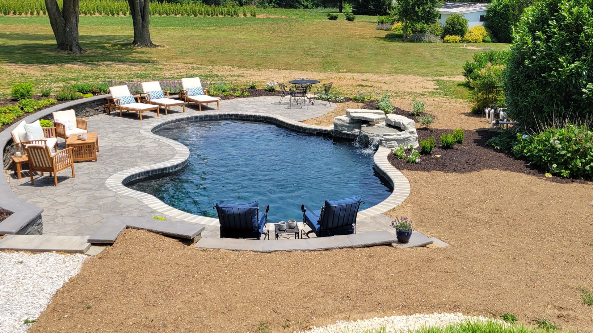 A large swimming pool is surrounded by chairs and a patio.