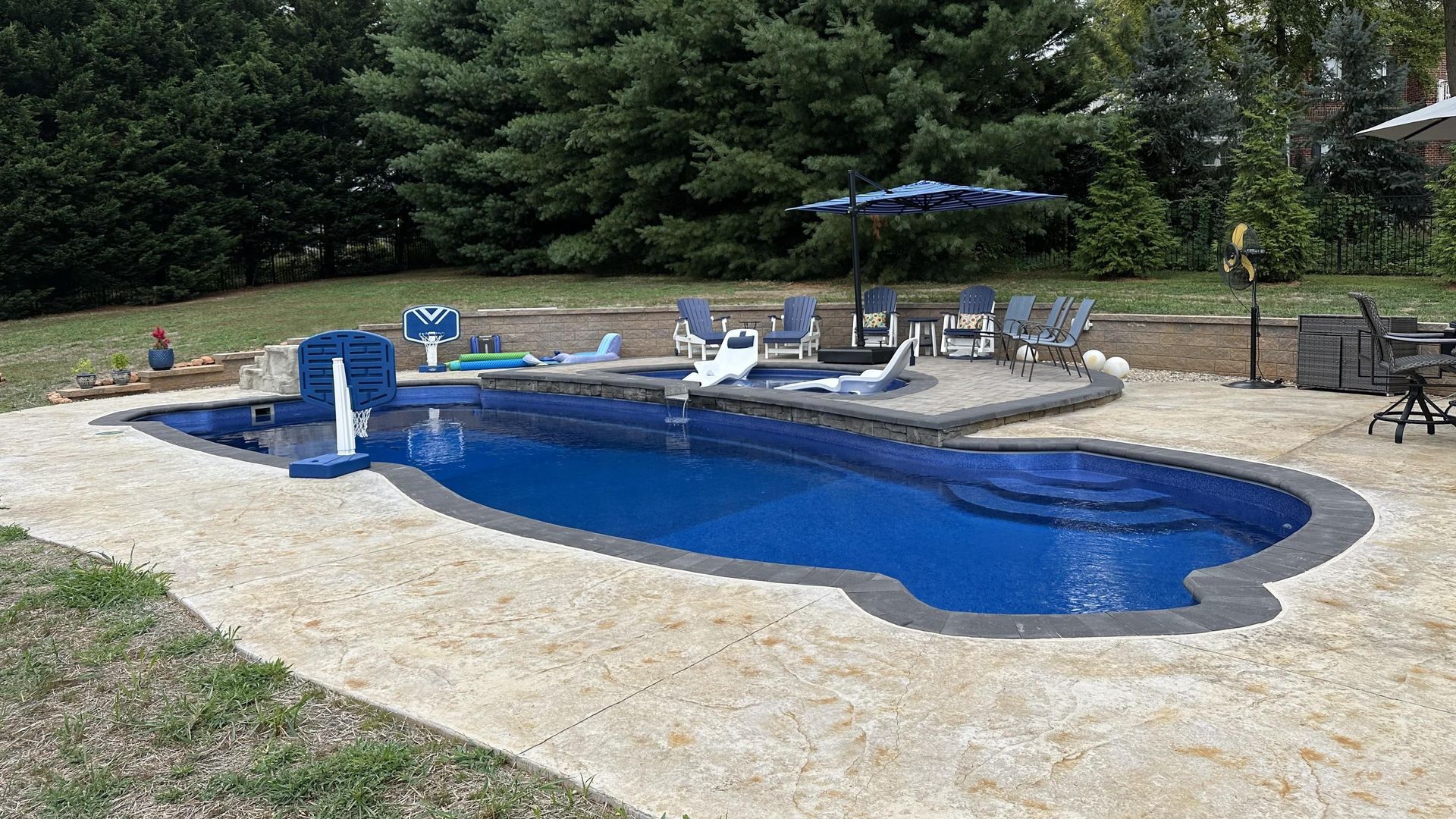 Backyard pool with blue water, lounge chairs, and stone deck surrounded by trees