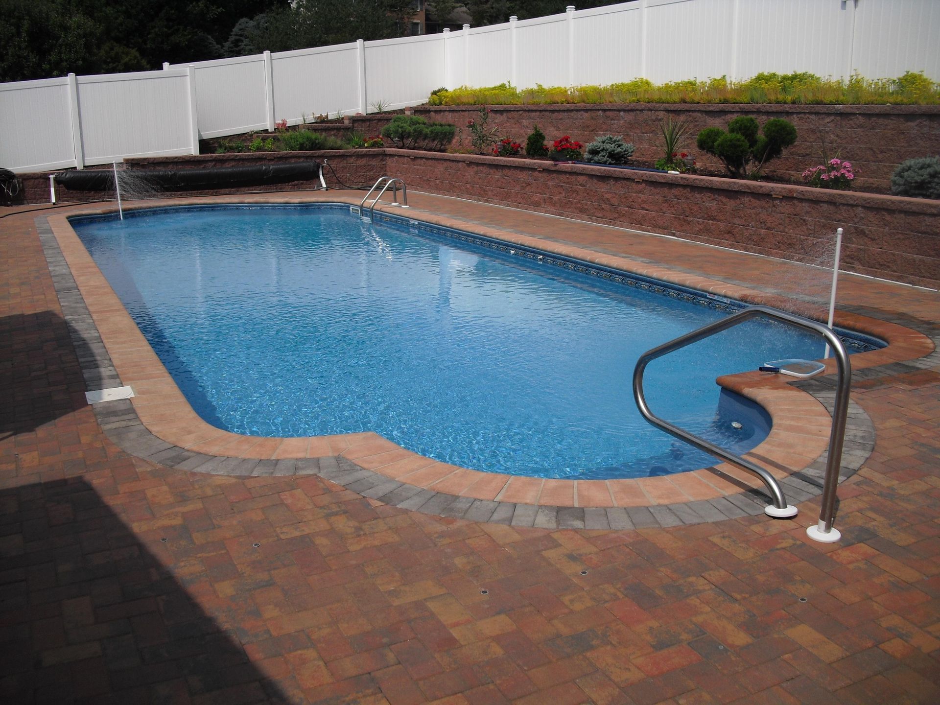 A large swimming pool is surrounded by bricks and a white fence.