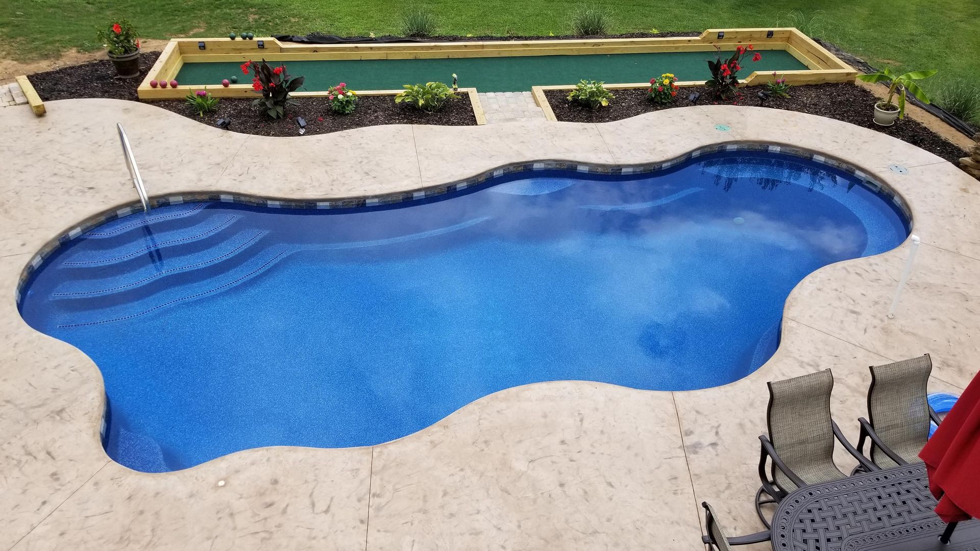 A large blue swimming pool is surrounded by chairs and a table.