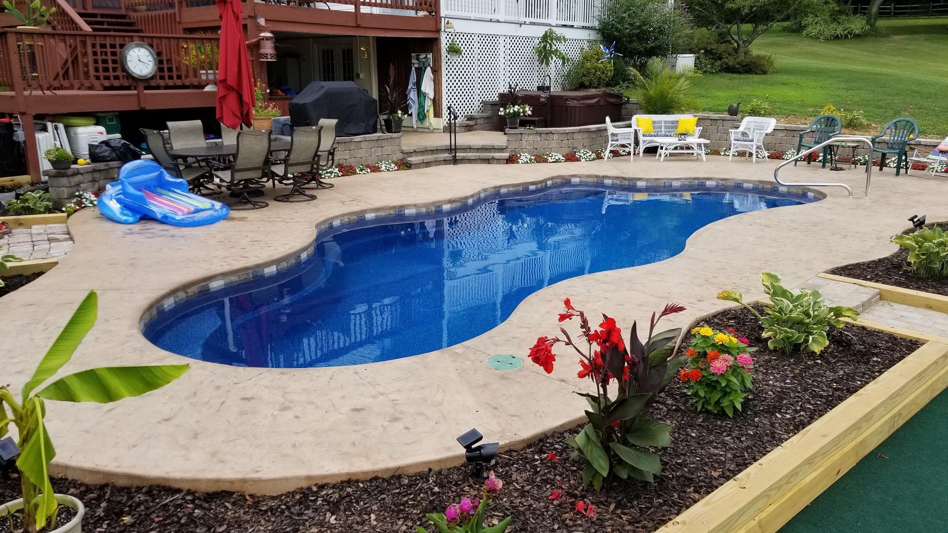 A large swimming pool is surrounded by flowers and a deck.