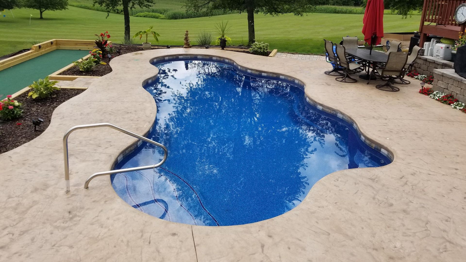 A large swimming pool is surrounded by a patio with a table and chairs.