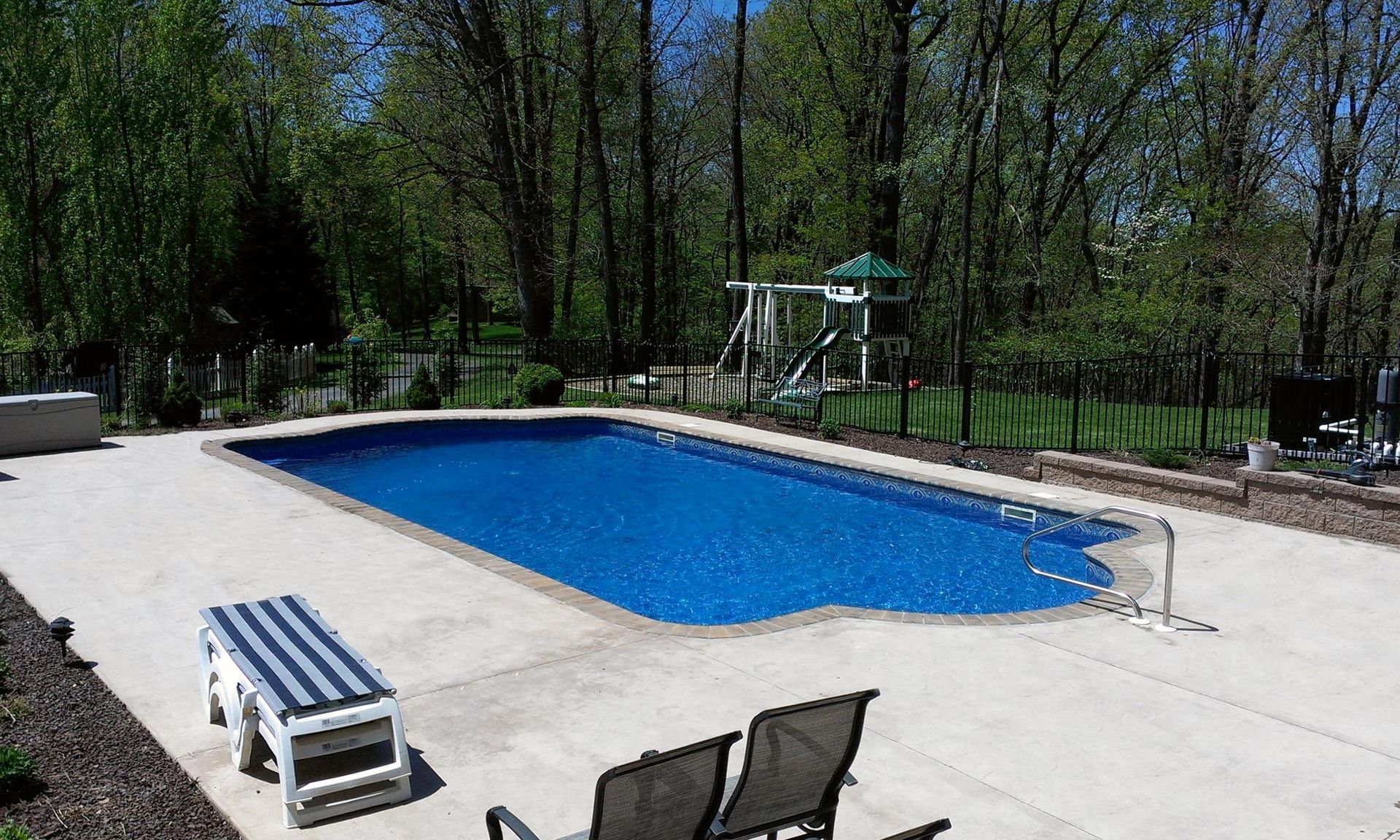 There is a large swimming pool in the backyard with a playground in the background.