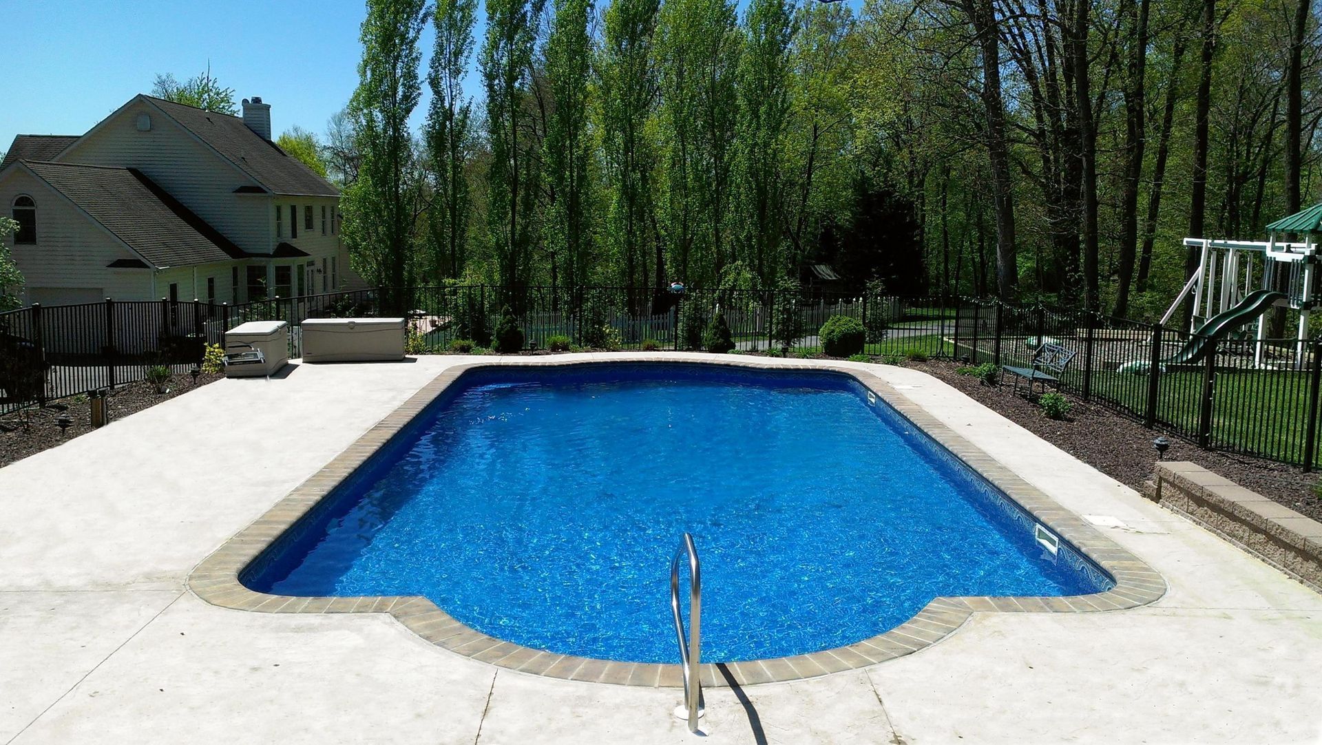 A large swimming pool is surrounded by trees and a house.
