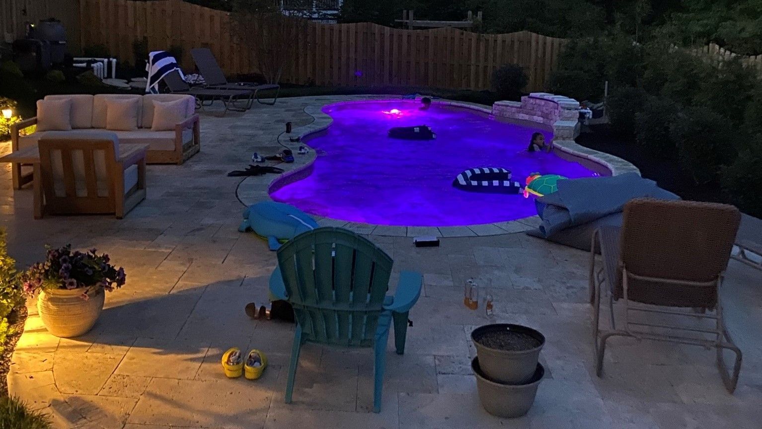 A large swimming pool is lit up with purple lights at night.