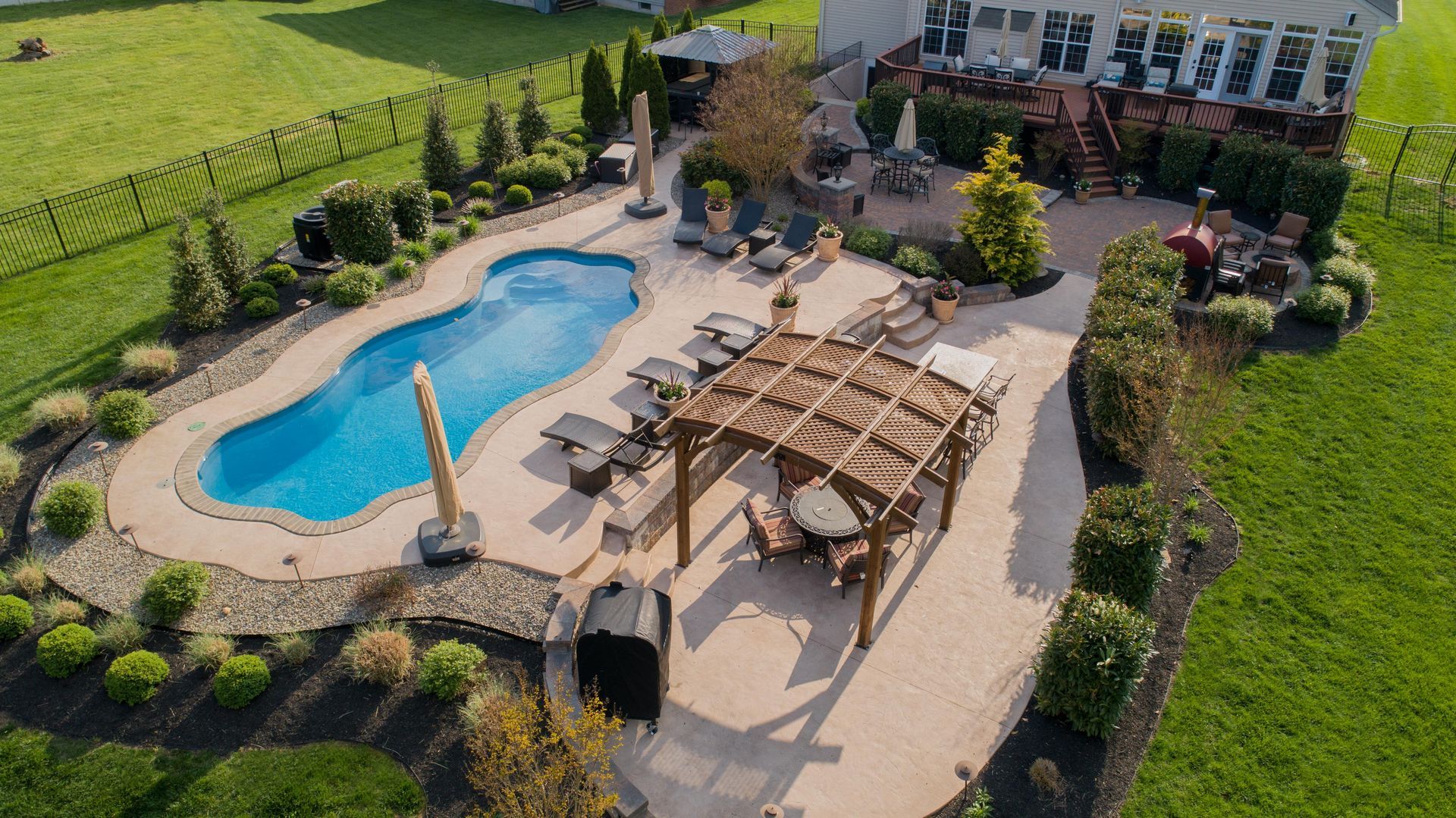 An aerial view of a backyard with a large swimming pool and a pergola.