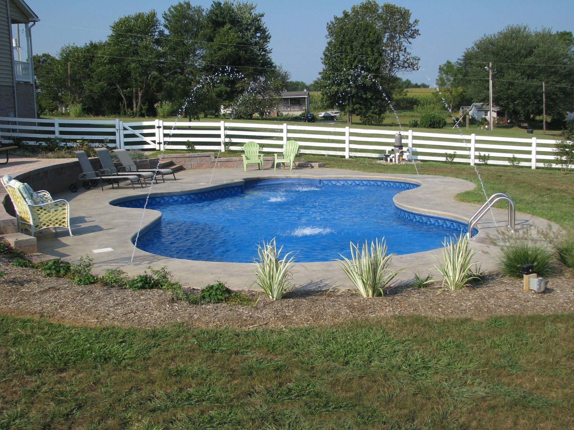 A large blue swimming pool surrounded by chairs and a white fence